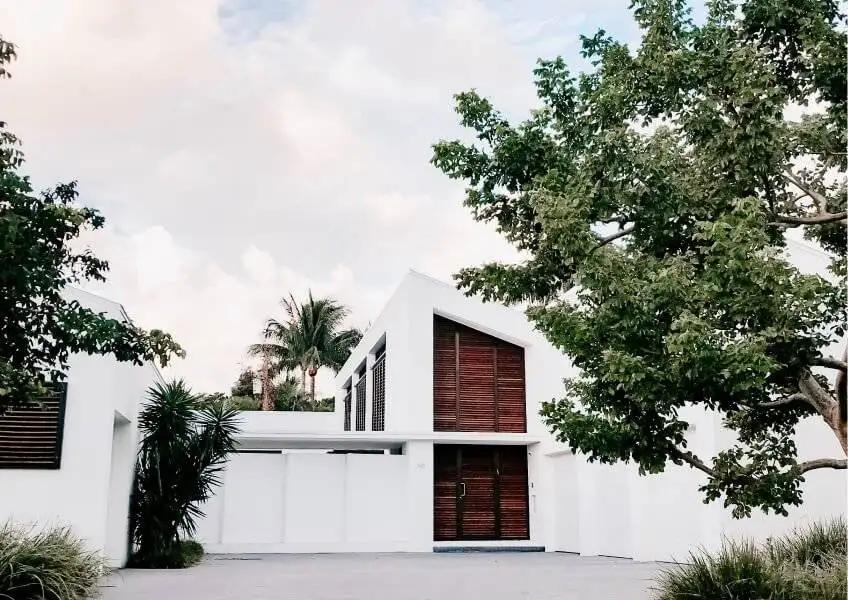 Modern white house with wooden accents surrounded by lush greenery, representing ideal real estate opportunities for buyers and sellers in Michigan.