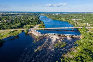 Aerial view of a river with a dam and lush greenery, highlighting the natural beauty of Mount Pleasant, Michigan, relevant to local real estate opportunities.