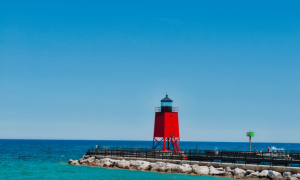 Red lighthouse on pier by blue water and clear sky in Loomis, MI, symbolizing local maritime heritage and real estate appeal.