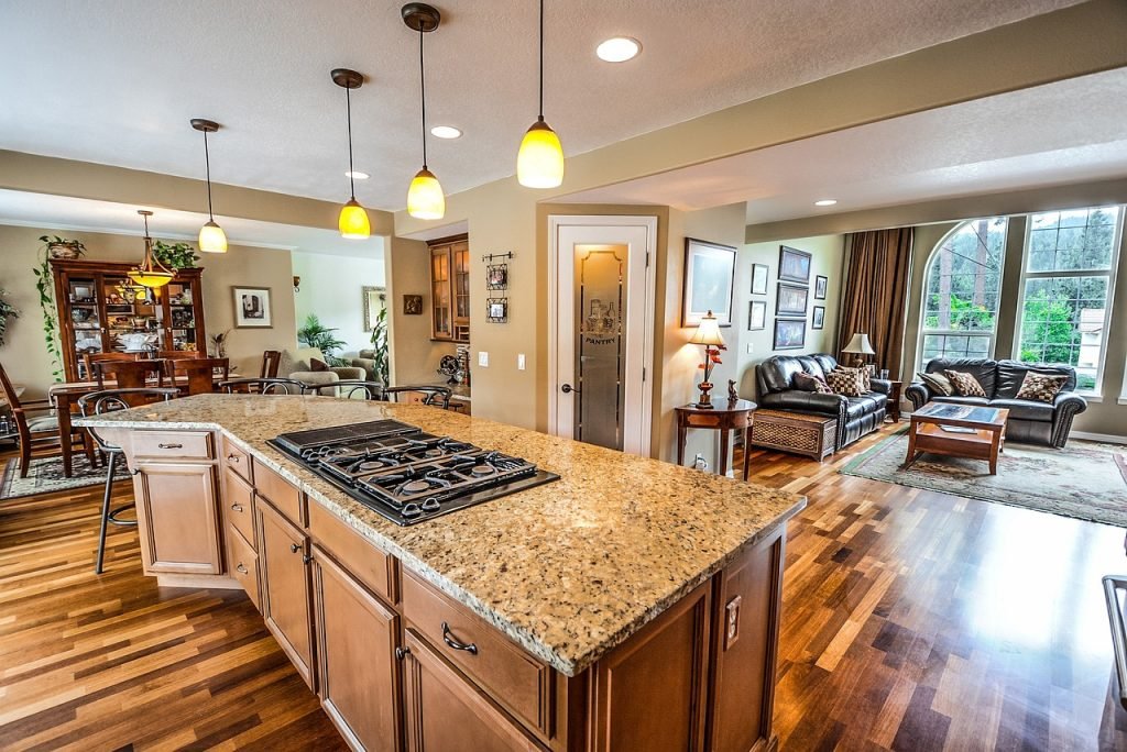 Modern kitchen with granite countertop and gas stove, open to living area featuring leather couches and large windows, highlighting spacious layout ideal for showcasing real estate properties.