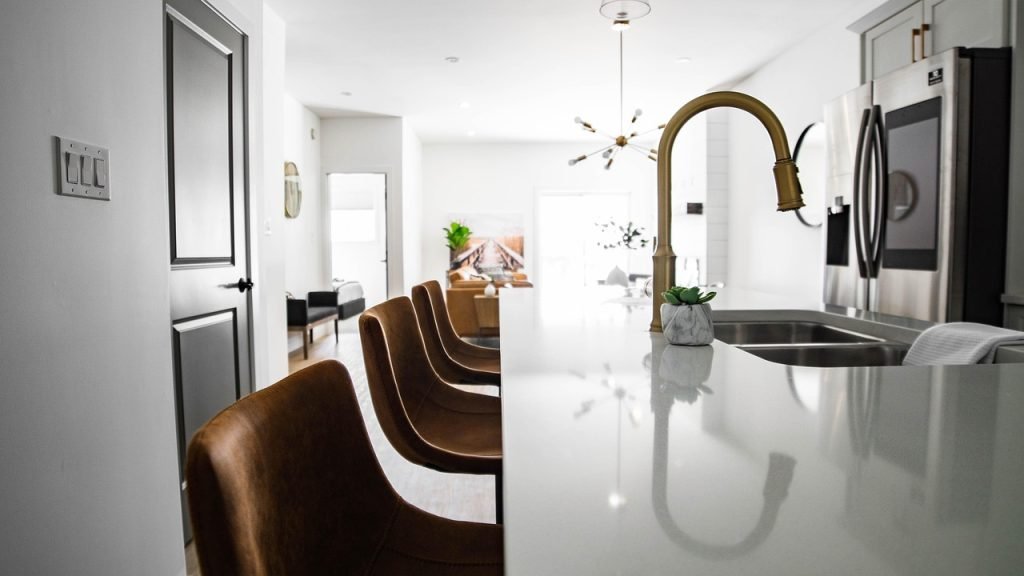 Modern kitchen interior featuring a sleek countertop, stylish brown chairs, a gold faucet, and a stainless steel refrigerator, emphasizing an inviting space for potential home buyers.