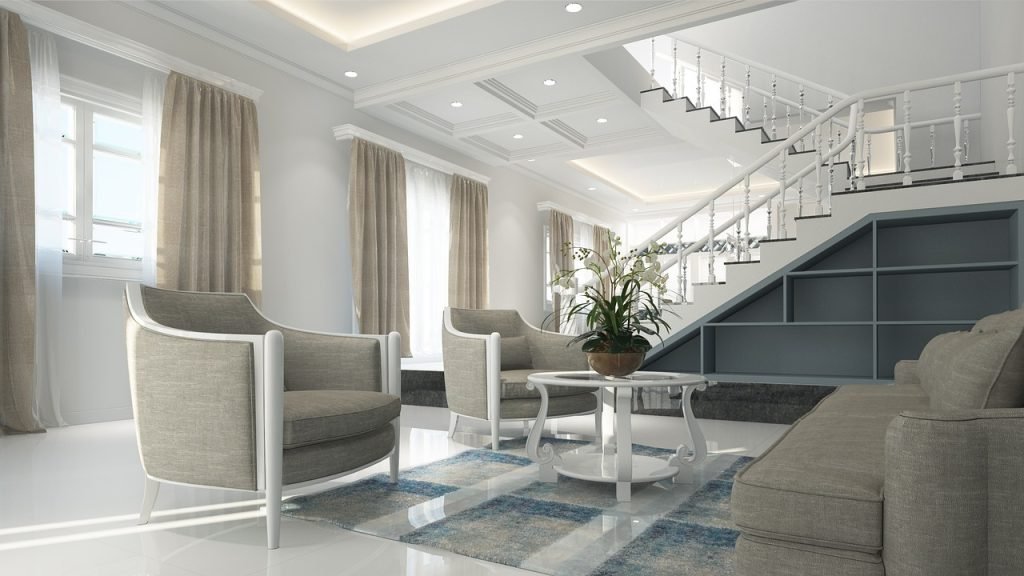Modern living room with gray armchairs, a round coffee table, and a decorative plant, showcasing an inviting atmosphere and elegant staircase, emphasizing home staging for real estate marketing.